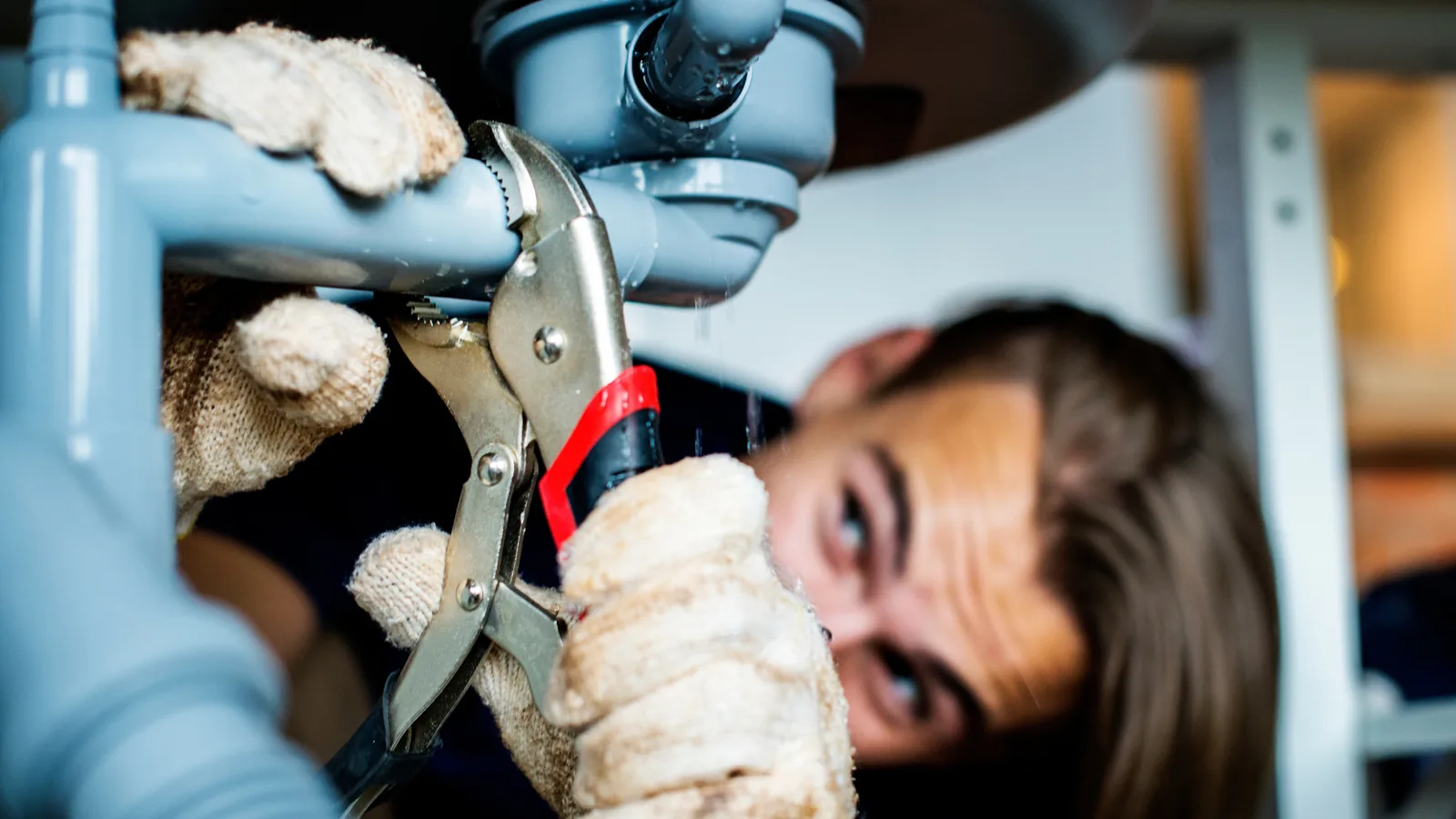 Licensed plumber tightening a pipe fitting under a sink