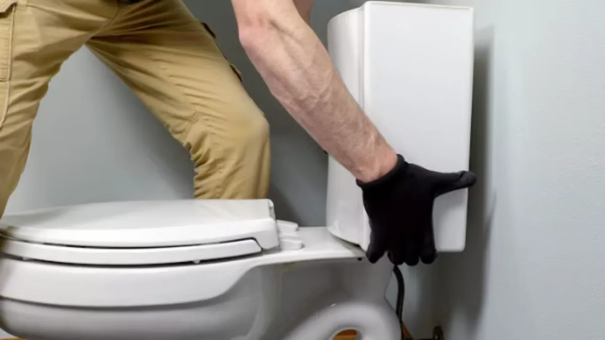 Technician servicing a toilet's tank and wall connection